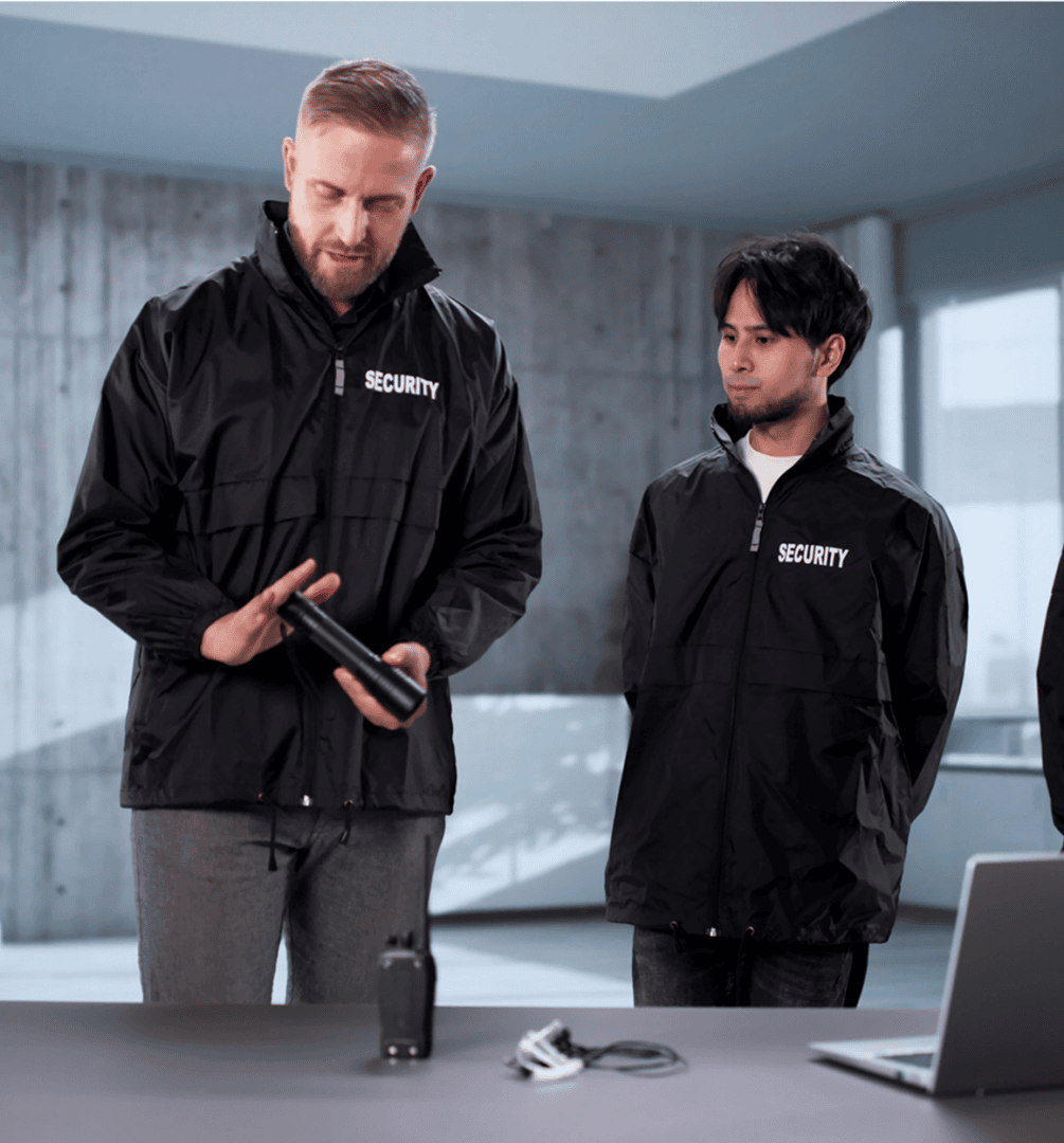 Two security guards discussing equipment indoors.