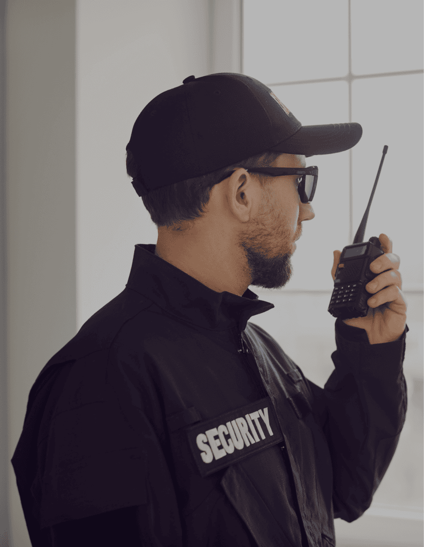 Security guard using walkie-talkie near window.